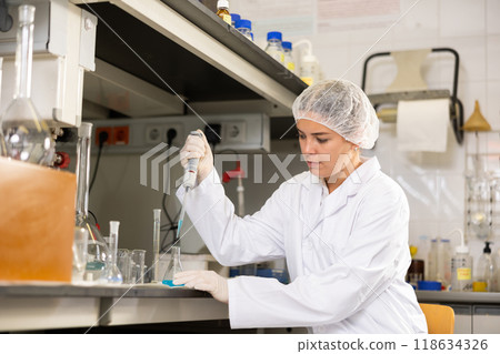 Researching in laboratory. Focused young female pipetting reagent into solution in test tube Researching in laboratory. Focused young female pipetting reagent into solution in test tube 118634326