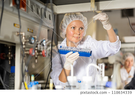 Female scientist researcher holding tripod and looking at reaction in test tube while performing biochemical tests in lab Female scientist researcher holding tripod and looking at reaction in test tube while performing biochemical tests in lab 118634339