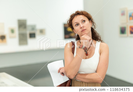 Middle-aged woman looking at pictures on wall in museum Middle-aged woman looking at pictures on wall in museum 118634375