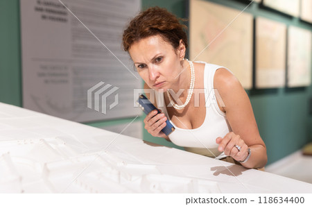 Middle-aged woman looking at building models in museum Middle-aged woman looking at building models in museum 118634400