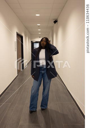 A successful businesswoman exuding confidence in a modern office hallway, dressed in stylish attire A successful businesswoman exuding confidence in a modern office hallway, dressed in stylish attire 118634436