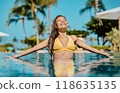 Summer sunbathing happy bikini woman swimming in infinity pool of luxury resort hotel relaxing on idyllic tropical travel vacation. Suntan solar skin care. 118635135