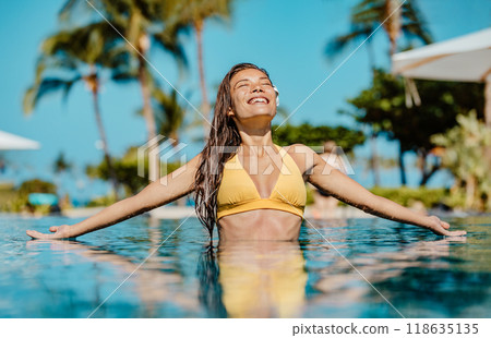 Summer sunbathing happy bikini woman swimming in infinity pool of luxury resort hotel relaxing on idyllic tropical travel vacation. Suntan solar skin care. 118635135
