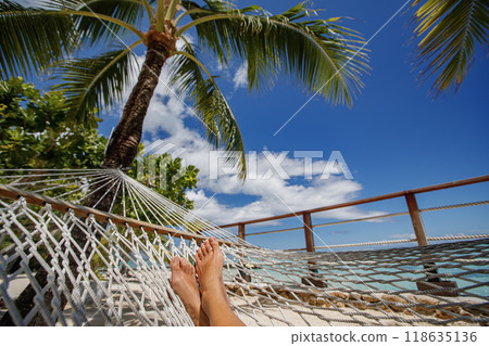 Beach travel holiday vacation woman feet selfie lying down relaxing on hammock outside sunbathing. Girl relaxing taking pov photo of her legs sun tanning in tropical summer destination 118635136