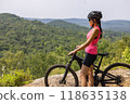 Woman on electric mountain bike in pink top, helmet and sunglasses, enjoying scenic forest view. eMTB concept 118635138