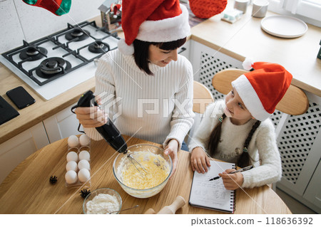 Mother and daughter baking together in festive Christmas kitchen Mother and daughter baking together in festive Christmas kitchen 118636392