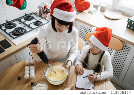 Mother and daughter baking together in Christmas hats Mother and daughter baking together in Christmas hats 118636394