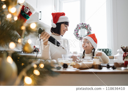 Mother and daughter baking Christmas cookies together in kitchen 118636410