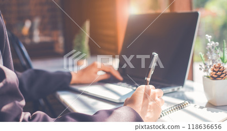 Woman hand writing on a notepad with a pen and use a laptop computer in the office.For web banner. Woman hand writing on a notepad with a pen and use a laptop computer in the office.For web banner. 118636656