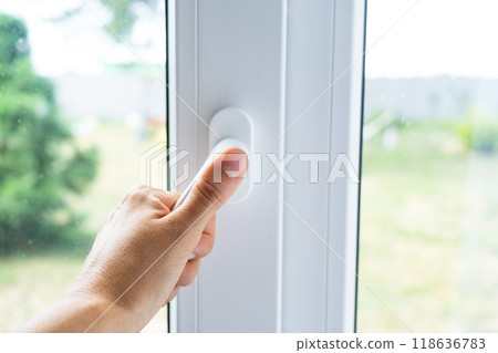 The hand holds the handle of a plastic double-glazed window, closing and opening the window with a rotary mechanism, the position of the handle for ventilation, micro-ventilation The hand holds the handle of a plastic double-glazed window, closing and opening the window with a rotary mechanism, the position of the handle for ventilation, micro-ventilation 118636783