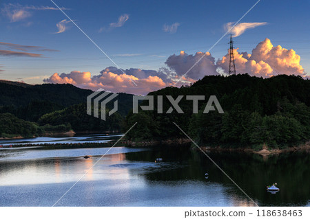 Early autumn evening view of Nunome Dam in the eastern part of Nara City. Cumulus clouds shining golden in the setting sun on the opposite side of the dam lake. Early autumn evening view of Nunome Dam in the eastern part of Nara City. Cumulus clouds shining golden in the setting sun on the opposite side of the dam lake. 118638463