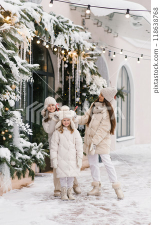 Young mother and daughters in winter clothes walk through the city decorated for Christmas Young mother and daughters in winter clothes walk through the city decorated for Christmas 118638768
