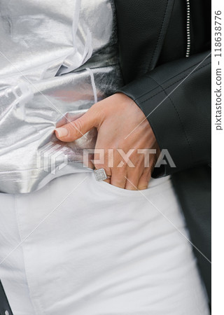 Woman is dressed in a silver black outfit and holds her hand in the pocket of her white trousers in close-up 118638776