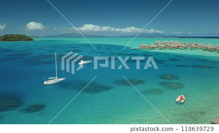 Two sailboats yachts anchor near shallow turquoise water lagoon near tropical island, luxury resort overwater bungalows in background. Maldives remote wild nature paradise, exotic summer luxury travel Two sailboats yachts anchor near shallow turquoise water lagoon near tropical island, luxury resort overwater bungalows in background. Maldives remote wild nature paradise, exotic summer luxury travel 118639729