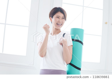 Middle-aged woman holding a yoga mat (fist pose) Middle-aged woman holding a yoga mat (fist pose) 118639861