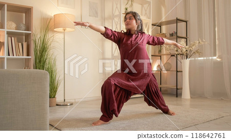 Yoga stretching. Healthy activity. Indoors training. Motivated woman practicing virabhadrasana warrior pose enjoying wellness at home in living room. Yoga stretching. Healthy activity. Indoors training. Motivated woman practicing virabhadrasana warrior pose enjoying wellness at home in living room. 118642761