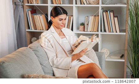 Home rest. Business woman. Research information. Elegant concentrated lady sitting sofa reading book in light room interior. 118642807