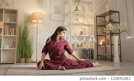 Yoga workout. Home training. Indoor activity. Flexible focused healthy woman stretching practicing pigeon pose exercise on floor in living room. Yoga workout. Home training. Indoor activity. Flexible focused healthy woman stretching practicing pigeon pose exercise on floor in living room. 118642861