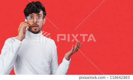 Mobile shock. Phone scam. Speaking anxiety. Scared overwhelmed confused man talking using gadget with omg reaction isolated on red empty space background. Mobile shock. Phone scam. Speaking anxiety. Scared overwhelmed confused man talking using gadget with omg reaction isolated on red empty space background. 118642863