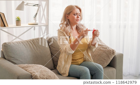 Pregnancy fail. Upset woman. Disappointment regret. Hopeful lady looking to result of medical test sitting light room interior. 118642979