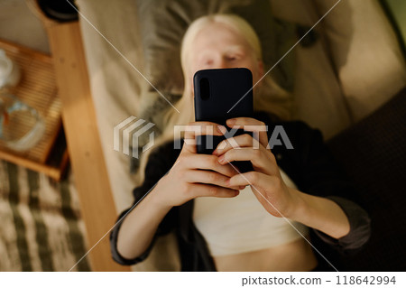 Unrecognizable girl with albinism taking selfie on smartphone while relaxing on sofa, from above view shot 118642994