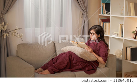 Book leisure. Reading evening. Home weekend. Peaceful young woman enjoying interesting novel story indoors relaxing on couch in living room copy space. Book leisure. Reading evening. Home weekend. Peaceful young woman enjoying interesting novel story indoors relaxing on couch in living room copy space. 118643013