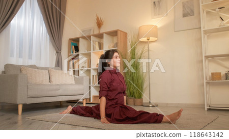 Stretching exercise. Home workout. Healthy lifestyle. Young sporty woman practicing legs front split training flexibility on floor in living room. Stretching exercise. Home workout. Healthy lifestyle. Young sporty woman practicing legs front split training flexibility on floor in living room. 118643142