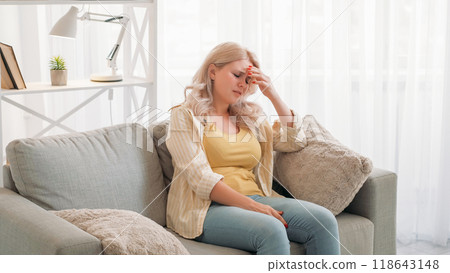 Upset woman. Disappointment regret. Headache suffer. Desperate lady expressing sadness holding head sitting light room interior. Upset woman. Disappointment regret. Headache suffer. Desperate lady expressing sadness holding head sitting light room interior. 118643148