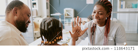 Doctor giving high-five to child during medical consultation as father watches proudly. Doctor smiling and showing support for child's achievement in healthcare setting Doctor giving high-five to child during medical consultation as father watches proudly. Doctor smiling and showing support for child's achievement in healthcare setting 118643171
