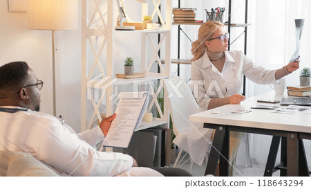 Clinical cooperation. Professional diagnostics. Healthcare work. Serious specialist doctor woman and man checking x ray film with medical history data at hospital office. 118643294