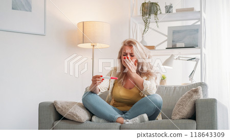 Unplanned pregnancy. Desperate woman. Sad emotion. Upset crying lady looking test result sitting sofa light room interior. 118643309