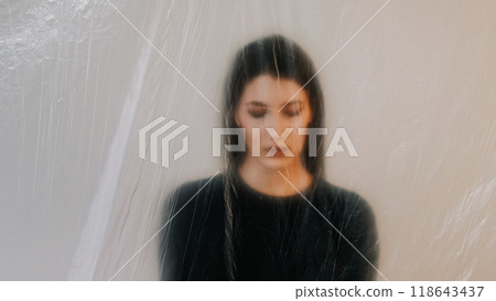 Depressed woman behind translucent plastic film veil evoking feelings of isolation solitude. 118643437
