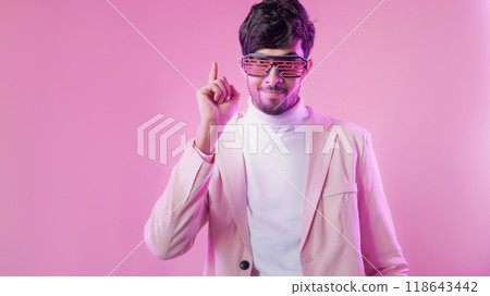 Party idea. Creative insight. Aha moment. Purple color neon light inspired man in glasses pointing finger up isolated on pink empty space background. Party idea. Creative insight. Aha moment. Purple color neon light inspired man in glasses pointing finger up isolated on pink empty space background. 118643442