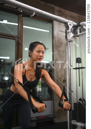 Young strong woman focusing on chest fly exercise in a gym. Sports and healthy lifestyle concept Young strong woman focusing on chest fly exercise in a gym. Sports and healthy lifestyle concept 118643709