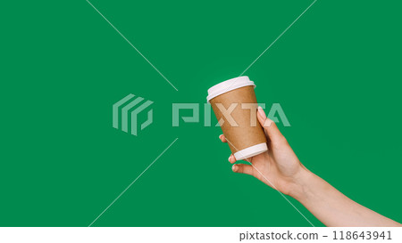 Coffee takeaway. Hot drink. Female hand offering brown eco mockup disposable cardboard paper cup isolated on green empty space background. Coffee takeaway. Hot drink. Female hand offering brown eco mockup disposable cardboard paper cup isolated on green empty space background. 118643941