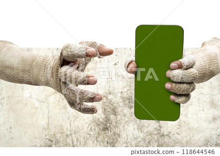 Mummy hands have dirty bandages on them. Mummy, devil, evil, satan, or zombie hands holding mobile phones or cell phones with green screens with a grungy wall background Mummy hands have dirty bandages on them. Mummy, devil, evil, satan, or zombie hands holding mobile phones or cell phones with green screens with a grungy wall background 118644546
