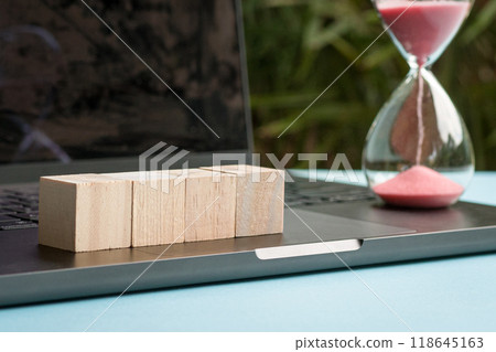 Four blank wood toy blocks in a row next to sand timer. 118645163