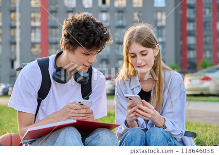 Teenage college students guy and girl talking, using smartphone, sitting outdoor Teenage college students guy and girl talking, using smartphone, sitting outdoor 118646038