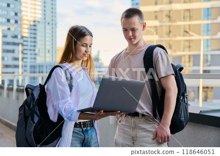 Talking teenage college age students looking at laptop screen, modern city background Talking teenage college age students looking at laptop screen, modern city background 118646051