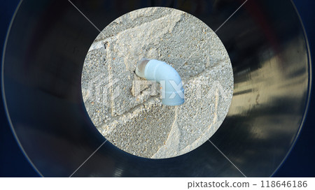 A clear view of a pipe fitting installed on a textured wall, showcasing the connection and structure against a bright backdrop. The setting appears outdoor with minimal shadows. 118646186