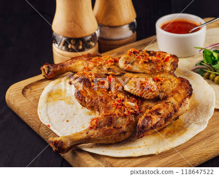 Roasted chicken lying on tortilla on wooden board with spices and sauce Roasted chicken lying on tortilla on wooden board with spices and sauce 118647522