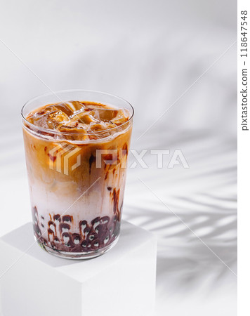 Iced coffee latte with chocolate syrup standing on white cube with tropical leaf shadow 118647548