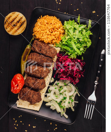 Delicious kofta kebabs served on pita bread with spices and vegetables on black plate 118647764