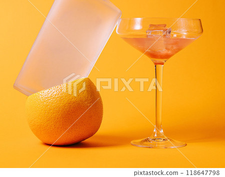 Frosted vodka bottle balancing on a grapefruit with cocktail glass on orange background 118647798