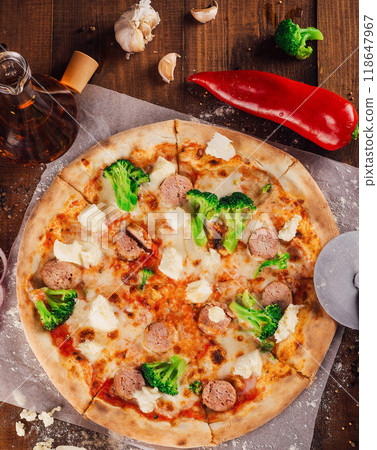 Delicious pizza lying on wooden table surrounded by fresh ingredients Delicious pizza lying on wooden table surrounded by fresh ingredients 118647967