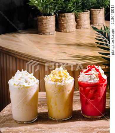 Three colorful milkshakes topped with whipped cream sitting on a cafe table Three colorful milkshakes topped with whipped cream sitting on a cafe table 118648012