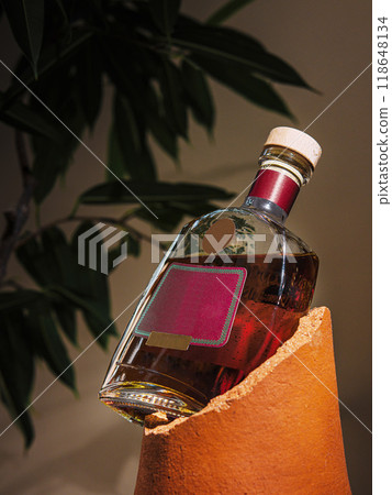 Bottle of cognac balancing precariously on edge of broken clay pot 118648134