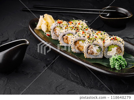 Sushi rolls covered with sesame seeds lying on a black plate on dark stone table 118648279