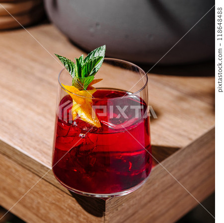 Red cocktail standing on wooden table with orange and mint garnish Red cocktail standing on wooden table with orange and mint garnish 118648488