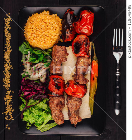 Grilled beef kebab served with bulgur, vegetables and peppers on black plate 118648498